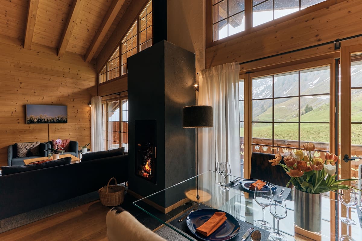 Una sala de estar acogedora con chimenea, un sofá, una mesa de centro de vidrio y vistas al exterior.