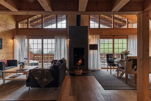 Un salon spacieux doté d’une cheminée, de parquets en bois et de grandes fenêtres.