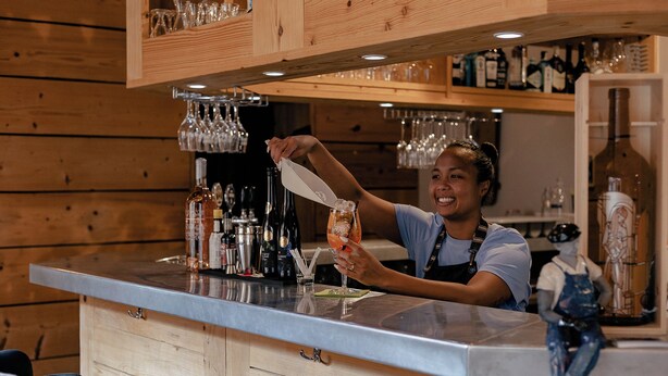 Eine Bar mit Holzsärchen, einer Theke und verschiedenen Flaschen und Gläsern.