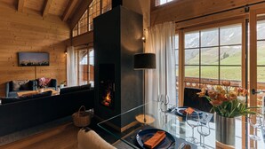 A cozy living room with a fireplace, a sofa, a glass coffee table, and a view of the outdoors. - Etable Des Crosets (Val d'Illiez)