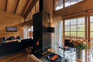 Una sala de estar acogedora con chimenea, un sofá, una mesa de centro de vidrio y vistas al exterior.