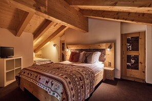 A bedroom with a wooden ceiling, a bed with patterned bedding, a bedside table, and a television. - Etable Des Crosets (Val d'Illiez)