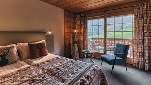 Ein Schlafzimmer mit einem großen Bett, einem Sessel, einem kleinen Tisch und einem Fenster mit Blick auf eine grüne Landschaft.