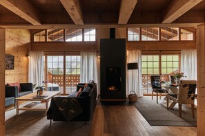 A wooden interior with a fireplace, a sofa, a dining table, and large windows. - Etable Des Crosets (Val d'Illiez)