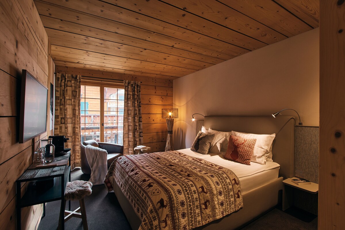 A wooden-paneled room with a bed, a desk, a chair, and a window with curtains.