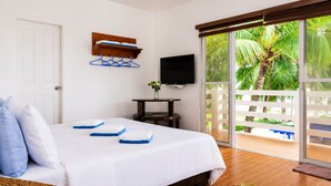 A hotel room with a bed, a television, a balcony with a view of palm trees, and a wicker chair.