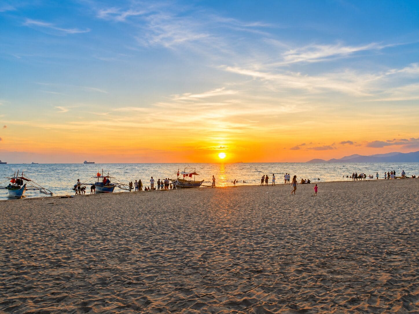 A beach at sunset with boats and people.