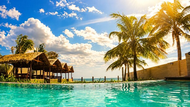 A clear pool with a thatched-roof structure and palm trees.