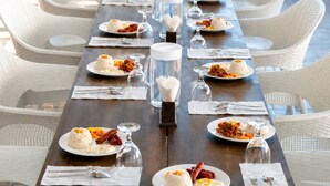 A long dining table with white chairs, set with plates of food, glasses, and cutlery.