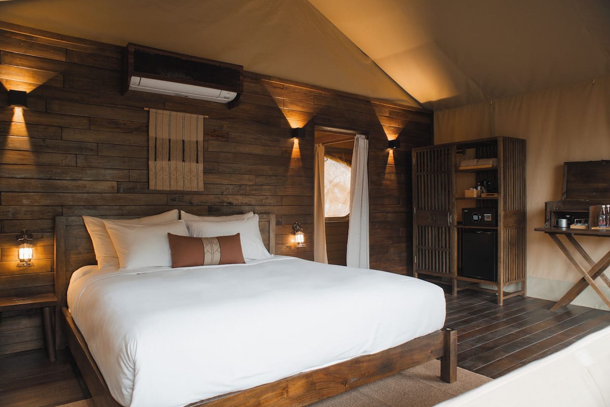 Ein Schlafzimmer mit Holzboden, einem Bett mit weißer Bettwäsche, einem Nachttisch mit Lampe und einer kleinen Küchenzeile.