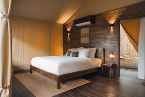 Ein Schlafzimmer mit einem Holzkopfteil, einem Bett mit weißer Bettwäsche, einem kleinen Nachttisch und einer Wand-Klimaanlage.