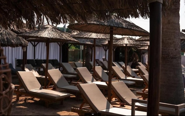 A beachside lounge area with thatched umbrellas and wooden lounge chairs. - Black And White Resort (Xylokastro-Evrostina)