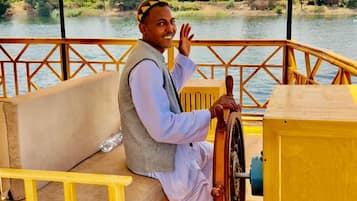 A person steering a boat on a wooden deck with a view of a river and greenery.