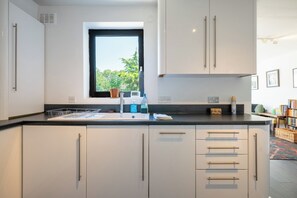 A modern kitchen with white cabinets, a black countertop, and a window providing natural light. - Peaceful 2BDR Escape Near Primrose Hill (Greater London)