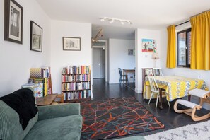 A living room with a sofa, a bookshelf, a dining table with chairs, and a kitchen area in the background. - Peaceful 2BDR Escape Near Primrose Hill (Greater London)