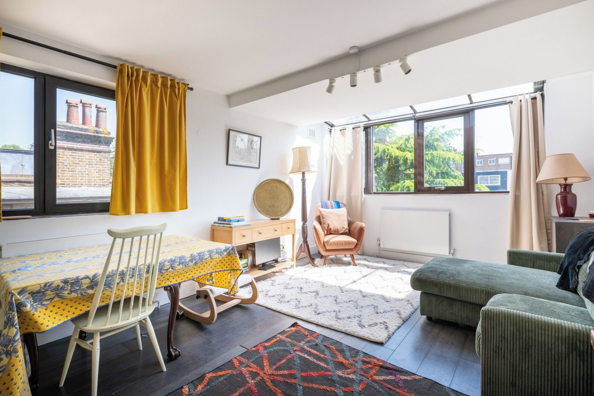 Ein Zimmer mit Esstisch, Stühlen, einer Couch, einer Lampe und Blick ins Freie.