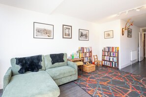 A living room with a green sofa, a bookshelf, and framed pictures on the wall. - Peaceful 2BDR Escape Near Primrose Hill (Greater London)