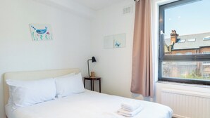 Et hotelværelse med en seng, et natbord, en lampe og et vindue med udsigt til bygninger.