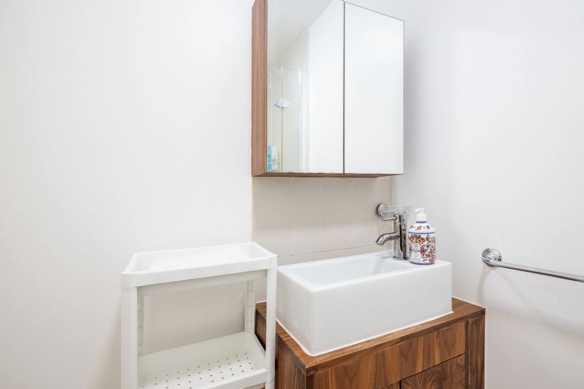Ein Badezimmer mit einem weißen Waschbecken, einem Spiegel darüber und einem Holzkabinet darunter.