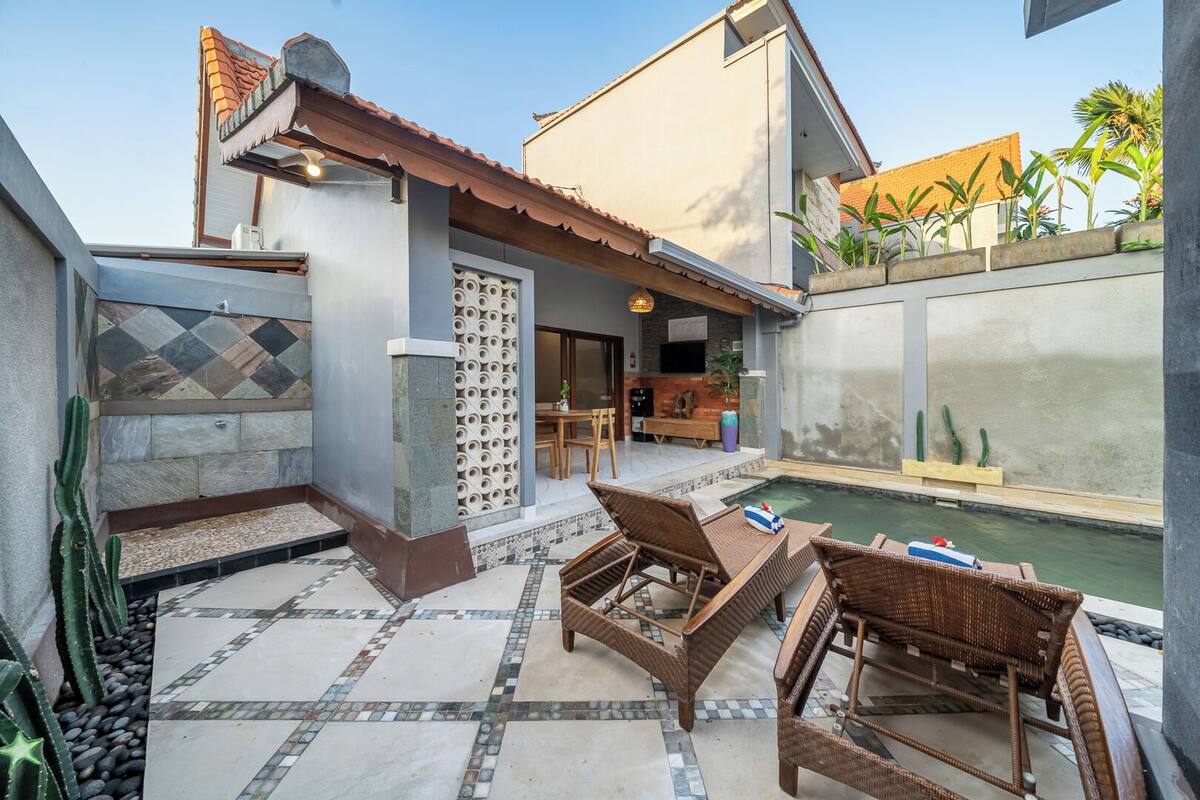 Une terrasse avec une piscine, des meubles en osier et un mur en pierre orné d’un motif décoratif.