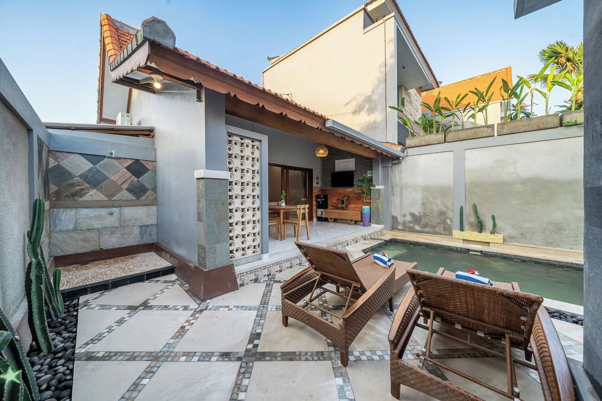 Une terrasse avec une piscine, des meubles en osier et un mur en pierre orné d’un motif décoratif.