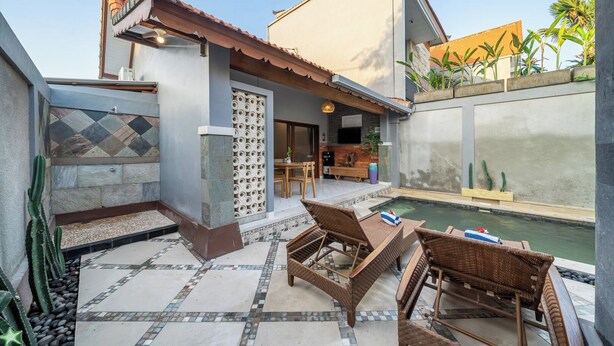 A patio with a pool, wicker furniture, and a stone wall with a decorative pattern. - Q~la Villas (Legian)