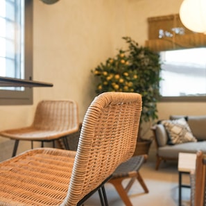 Korbstühle mit gewebter Textur, eine Couch und ein Blumentopf mit gelben Blüten in einem Zimmer mit Fenster und Lampe.