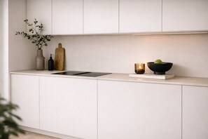 Eine moderne Küche mit weißen Schränken, einer schwarzen Arbeitsplatte, einer Vase mit grünen Blättern, einem Holzbruchbrett, einer Kerze und einer Schüssel mit Obst.