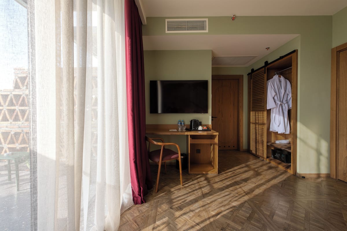 Habitación de hotel con un escritorio de madera, televisión, bata colgada y vistas a través de una ventana con cortinas.