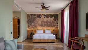Un dormitorio con una cama, un ventilador de techo, una mesita de noche de madera, una silla, un sofá y un mural en la pared.