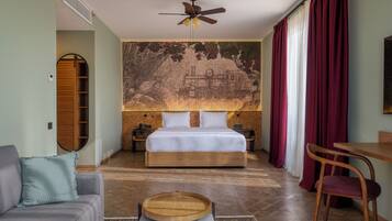 Une chambre à coucher comprenant un lit, un ventilateur de plafond, une table de chevet en bois, une chaise, un canapé et une fresque murale.