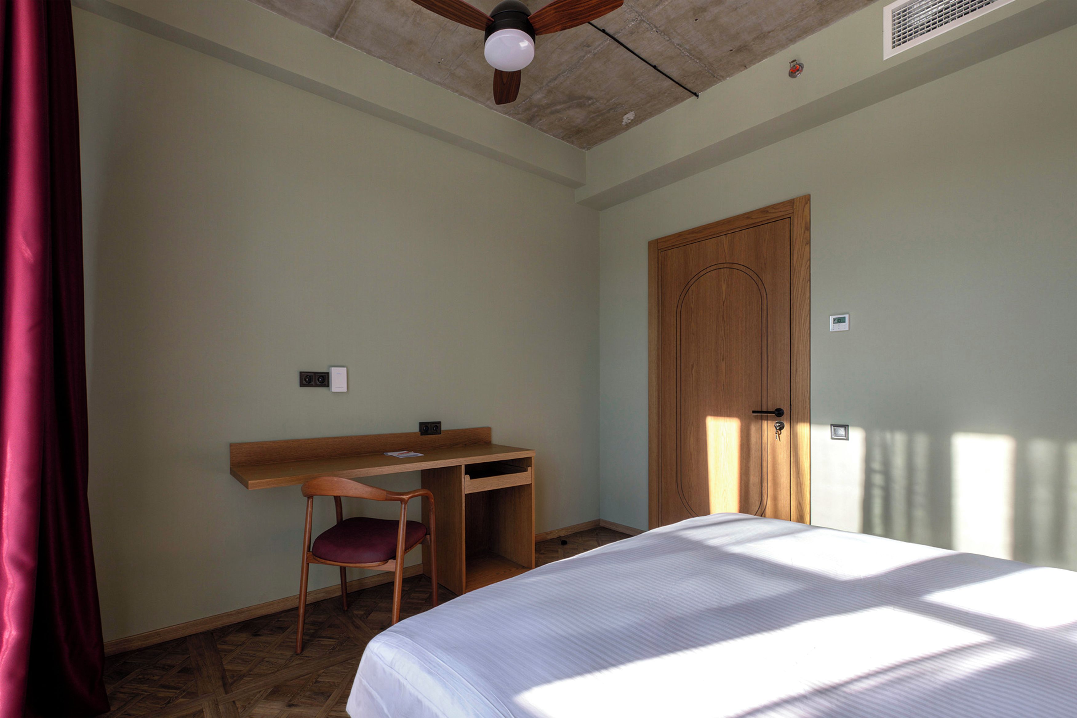 Um quarto com cama, escrivaninha, cadeira e porta.