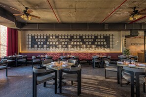 Un restaurante con mesas y sillas, una pared con diseños circulares y una zona de recepción.