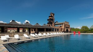 Una piscina con sillas de descanso, un edificio de ladrillo con una torre y un cielo azul despejado.