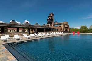 A pool with lounge chairs, a brick building with a tower, and a clear blue sky.