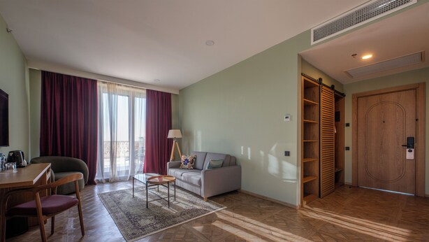 Una sala de estar con sofá, una mesa de centro, televisión, comedor con sillas, una puerta de madera y una ventana con cortinas.