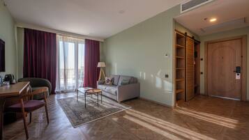 Un salon comprenant un canapé, une table basse, un téléviseur, un coin repas avec des chaises, une porte en bois et une fenêtre avec des rideaux.