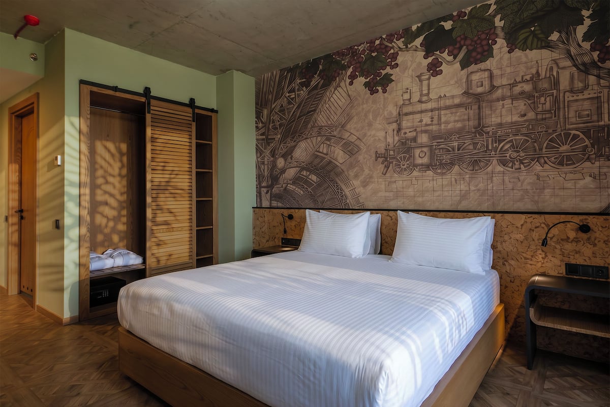 Habitación de hotel con una cama grande, un armario de madera y un mural de un tren en la pared.