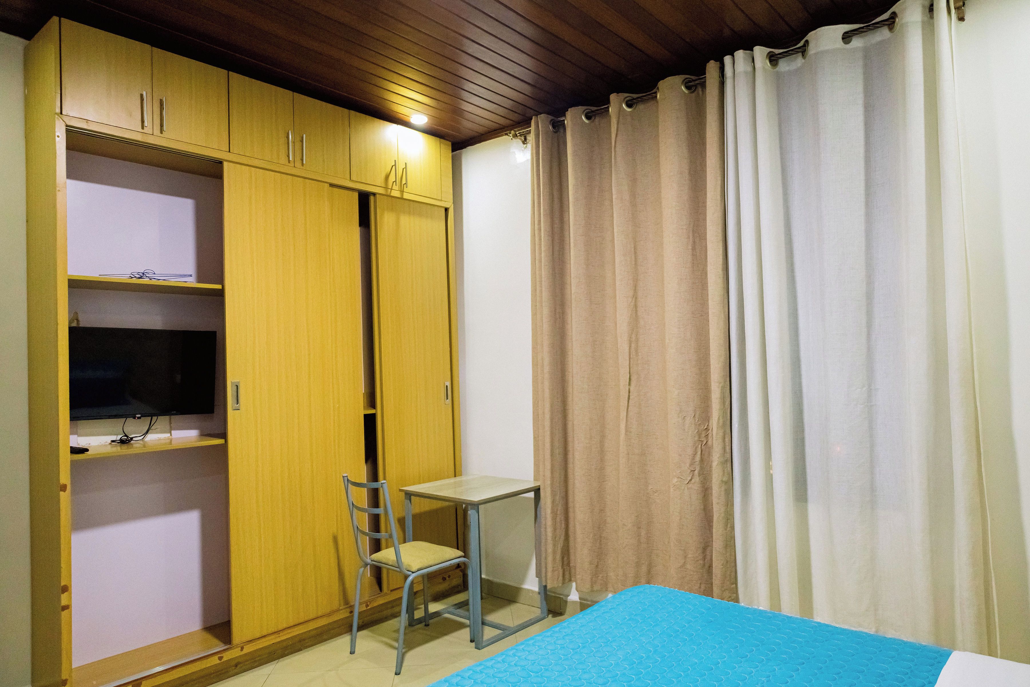 Una habitación con una cama, un escritorio, una silla, un televisor en un estante y un armario.