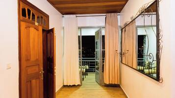 A hallway with a wooden door, a glass door leading to a balcony, and a metal railing.