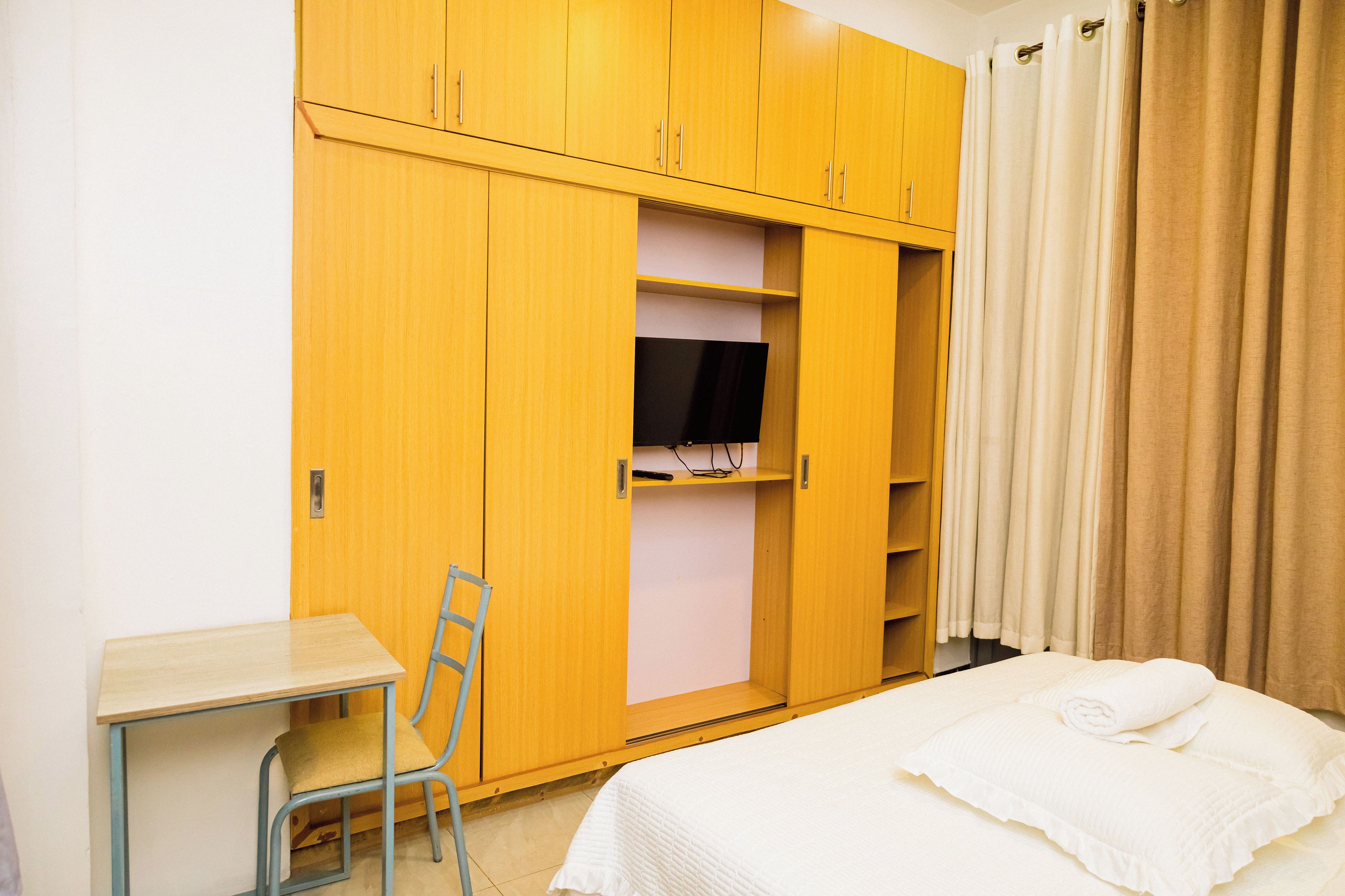 A hotel room with a bed, a desk, a chair, a wardrobe, and a television.