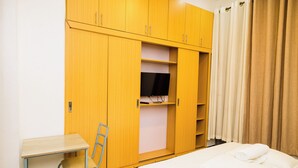 A hotel room with a bed, a desk, a chair, a wardrobe, and a television. - Poolside Viewbguesthouse (Kigali)