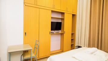 A hotel room with a bed, a desk, a chair, a wardrobe, and a television.