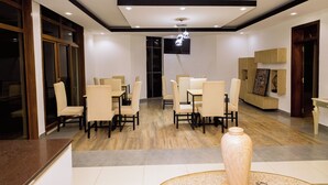 A modern dining area with wooden flooring, beige chairs, and a central table. - Poolside Viewbguesthouse (Kigali)