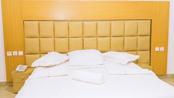 A neatly made bed with a headboard, a bedside phone, and a painting above it.