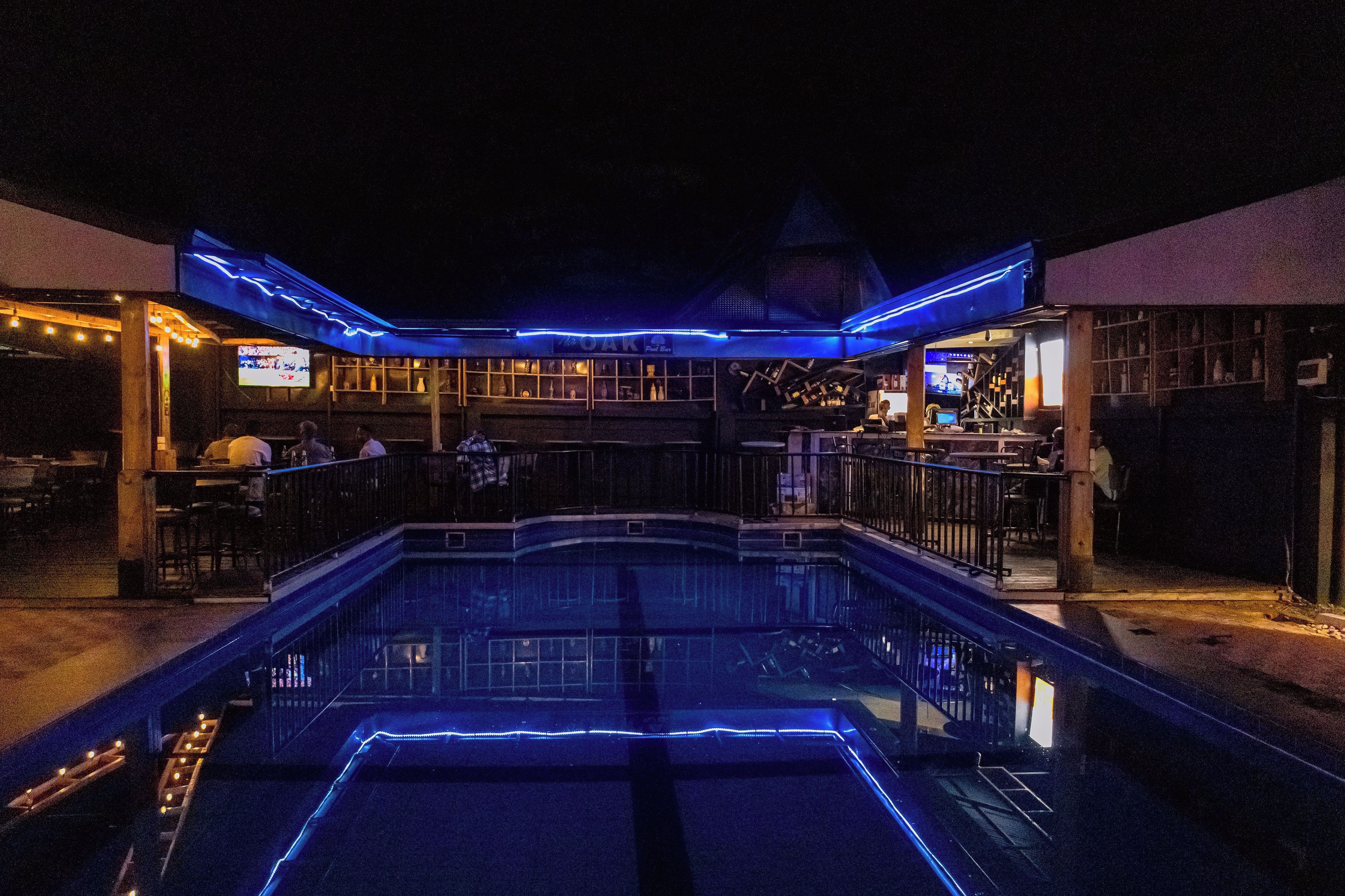 Un área de piscina con bar y asientos, rodeada por un edificio con una estructura de techo distintiva.