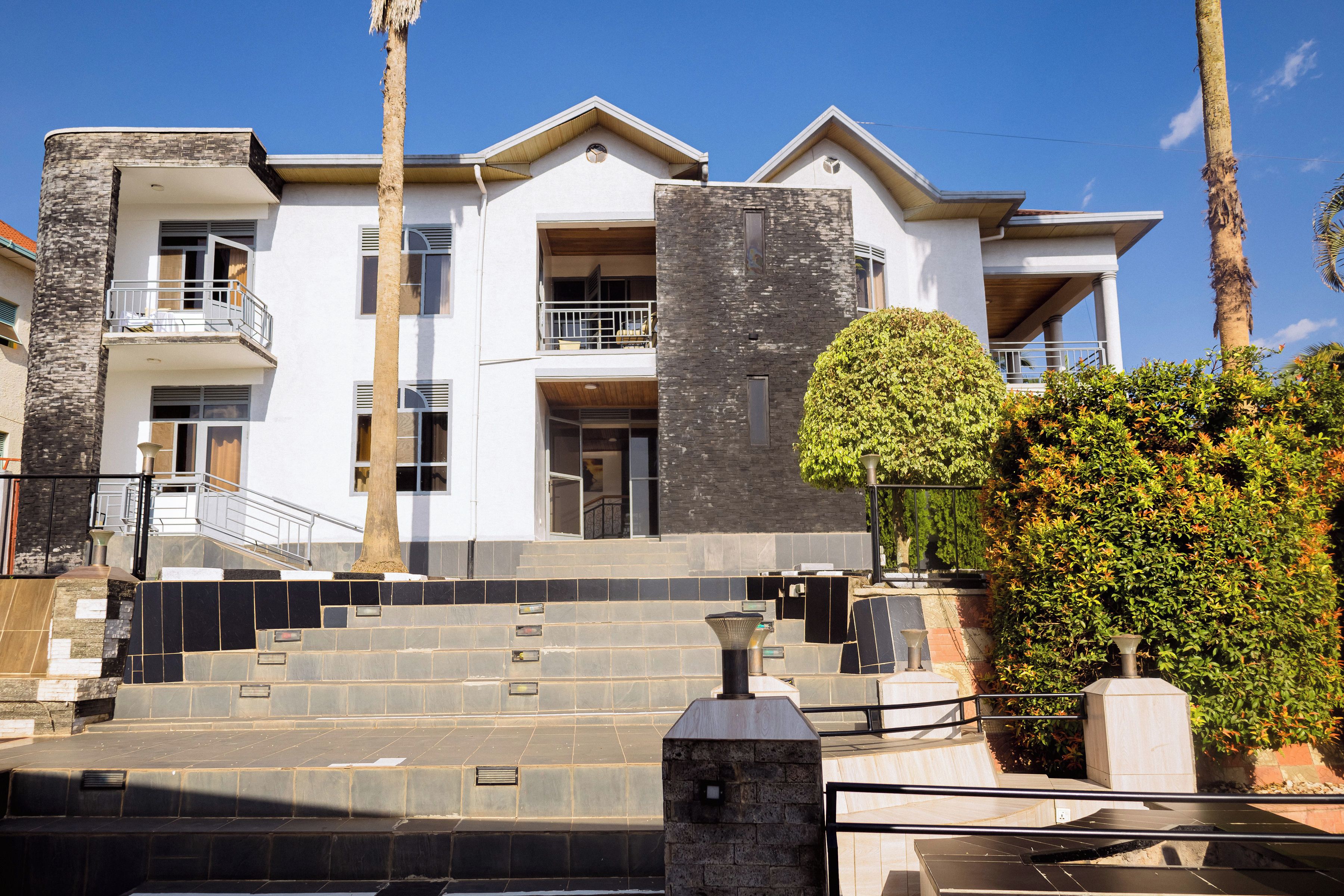 A multi-story residential building with a stone facade, a balcony, and a well-maintained garden.