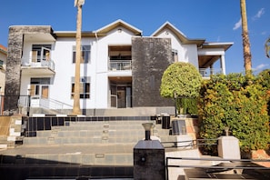 A multi-story residential building with a stone facade, a balcony, and a well-maintained garden. - Poolside Viewbguesthouse (Kigali)