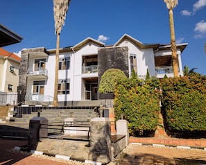 A multi-story building with balconies, a stone staircase, and a well-maintained garden. - Poolside Viewbguesthouse (Kigali)