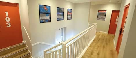 A hotel hallway with a staircase, white railings, and numbered doors.